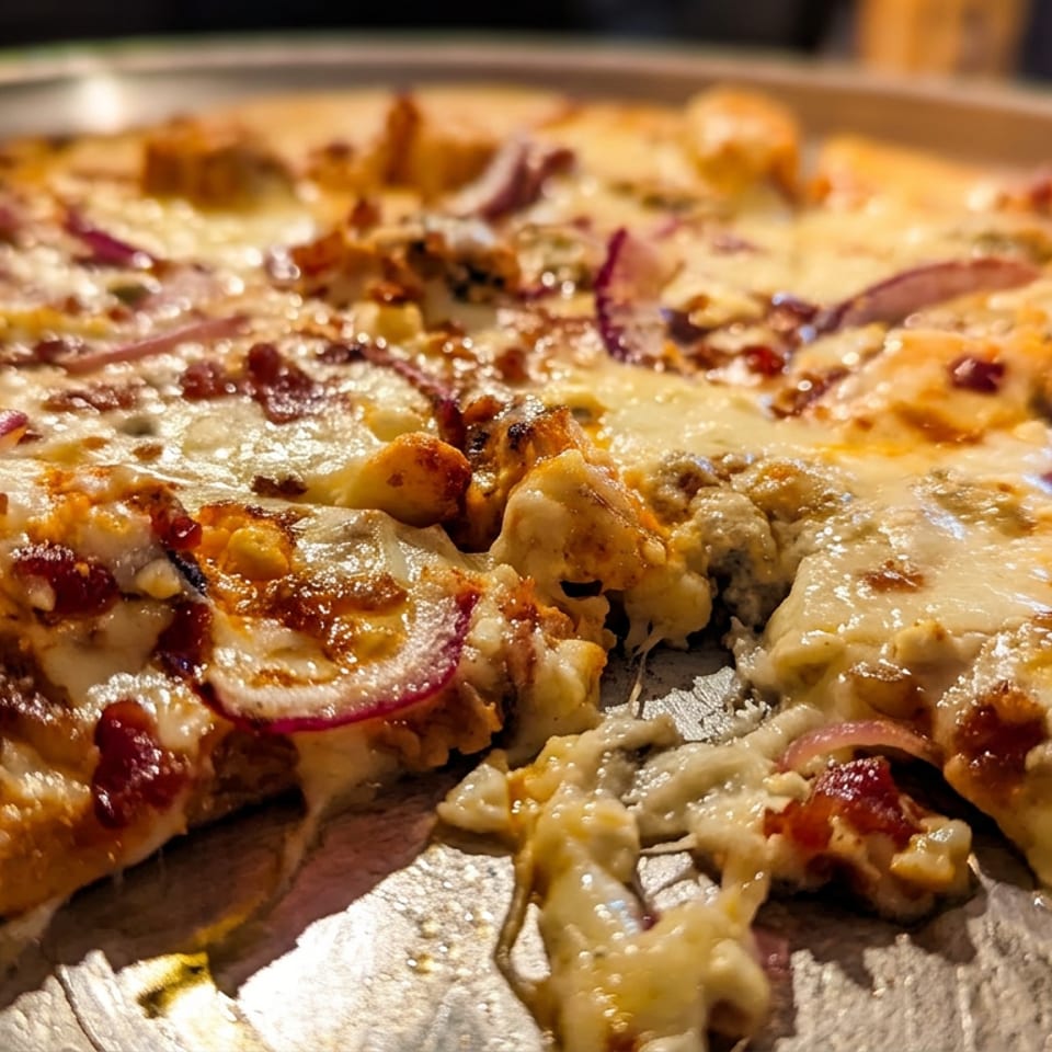 Close-up of a pizza with melted cheese, red onions, and chicken, with a slice removed.