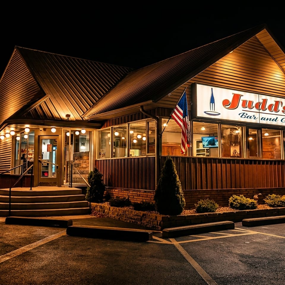 Judd's Bar and Grille exterior at night, illuminated with warm lights and an American flag.