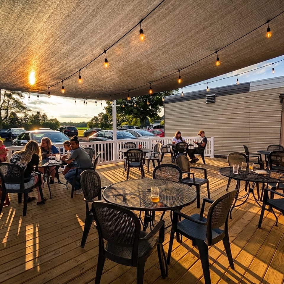 People dining on a restaurant's outdoor patio under a shaded canopy with string lights at sunset.