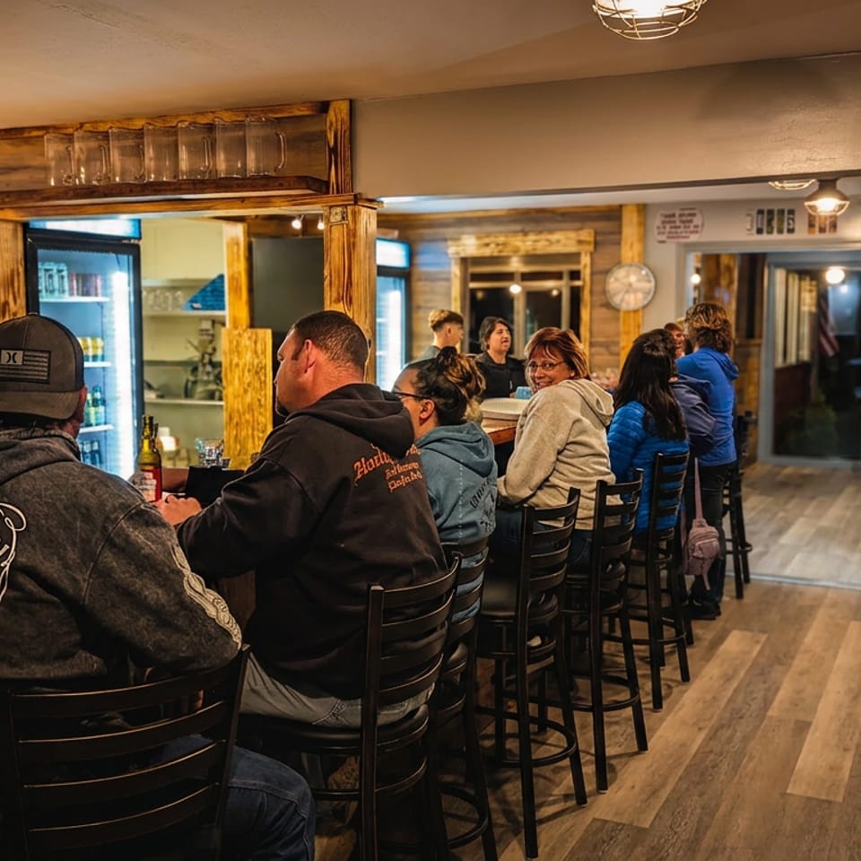 Patrons seated at a rustic wooden bar, enjoying drinks in a warmly lit restaurant interior.