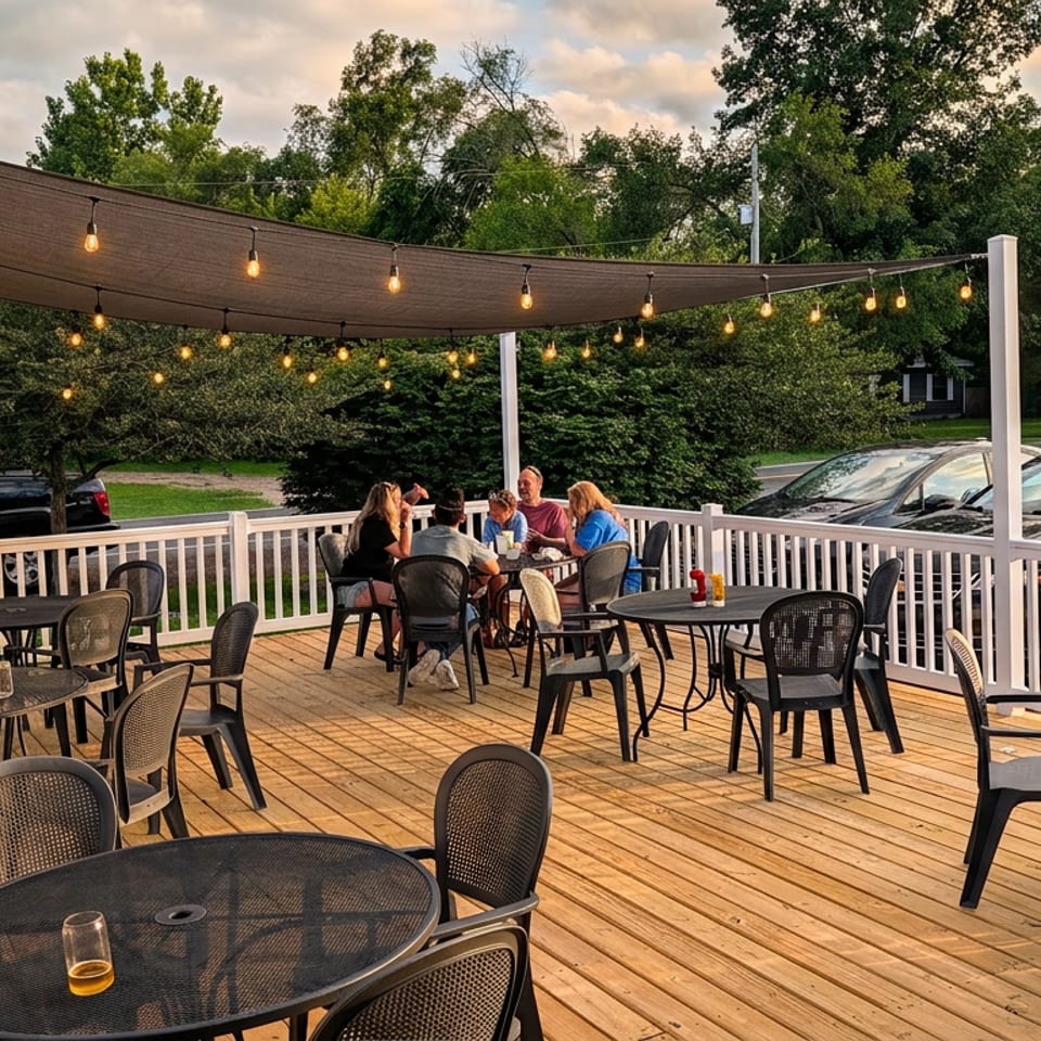 Patrons enjoy dining on a spacious outdoor wooden deck with string lights and lush green trees.